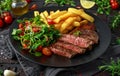 Grilled sirloin steak with potato fries and vegetables, tomato salad in a black plate. rustic table Royalty Free Stock Photo