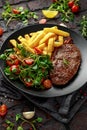 Grilled sirloin steak with potato fries and vegetables, tomato salad in a black plate. rustic table Royalty Free Stock Photo