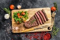 Grilled sliced Denver steak on a cutting board. BBQ beef. Black background. Top view