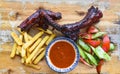 Grilled smoked pork ribs with french fries and sauce and salad on wooden board on black background top view Royalty Free Stock Photo