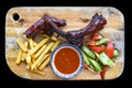 Grilled smoked pork ribs with french fries and sauce and salad on wooden board on black background top view Royalty Free Stock Photo