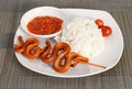 Grilled snake on skewer with chili sauce and rice on white plate on mat