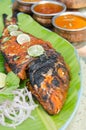 Grilled spicy fish tikka served with mint, lime, sauces and a banana leaf in a rustic setting