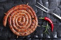 Grilled spiral sausages on a black background of charcoal.