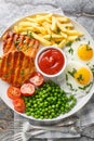 Grilled steak with green peas, fried egg, french fries, tomatoes and sauce close-up in a plate. Vertical top view Royalty Free Stock Photo