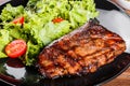 Grilled steak meat with fresh vegetable salad and tomatoes on black plate, wooden background. Royalty Free Stock Photo