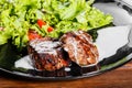 Grilled steak meat with fresh vegetable salad, tomatoes and sauce on black plate, wooden background. Royalty Free Stock Photo