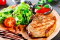 Grilled steak pork with fresh vegetable salad, tomatoes and sauce on wooden cutting board