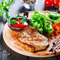 Grilled steak pork with fresh vegetable salad, tomatoes and sauce on wooden cutting board. Hot Meat Dishes. Royalty Free Stock Photo