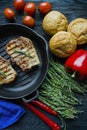 Grilled steak on a round grill pan, garnished with spices for meat, rosemary, greens and vegetables on a dark wooden background Royalty Free Stock Photo