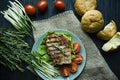 Grilled steak served on a plate, decorated with spices for meat, rosemary, greens and vegetables on a dark wooden background Royalty Free Stock Photo