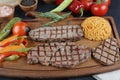 Grilled T-bone steak seasoned with spices and fresh herbs served on a wooden board with fresh tomato , fried vegetables, tomatoes, Royalty Free Stock Photo