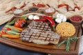 Grilled T-bone steak seasoned with spices and fresh herbs served on a wooden board with fresh tomato , fried vegetables, tomatoes, Royalty Free Stock Photo