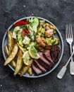 Grilled tapas food - beef steak, baked potatoes, vegetable salad, chicken with zucchini on a dark background, top view Royalty Free Stock Photo