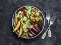 Grilled tapas food - beef steak, baked potatoes, vegetable salad, chicken with zucchini on a dark background, top view Royalty Free Stock Photo