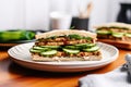 grilled tempeh sandwich with pickles on a round plate