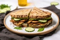 grilled tempeh sandwich with pickles on a round plate