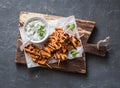 Grilled teriyaki chicken skewers and tzatziki sauce on a wooden board on a dark background, top view.