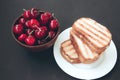 Grilled toast sandwich with egg on plate and red cherries in a cup