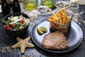 Grilled tuna steak served with potato fries in a metal serving basket and salad mix, on black plates, selective focus. Royalty Free Stock Photo