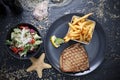 Grilled tuna steak served with potato fries in a metal serving basket and salad mix, on black plates, top view. Royalty Free Stock Photo