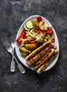 Grilled turkey sausages and roasted vegetables on a dark background, top view. Delicious lunch, tapas, appetizer
