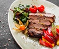 Grilled veal steak with salad and vegetables in plate on dark stone background. Hot Meat Dishes, top view