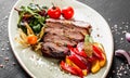 Grilled veal steak with salad and vegetables in plate on dark stone background. Hot Meat Dishes, top view Royalty Free Stock Photo