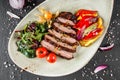 Grilled veal steak with salad and vegetables in plate on dark stone background. Hot Meat Dishes, top view Royalty Free Stock Photo