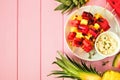 Grilled summer watermelon and pineapple fruit kabobs, top view side border on a pink wood background