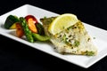 Grilled zander fillet with mixed grilled vegetables on white rectangular plate. Black background
