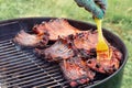 Grilling pork ribs on a round barbecue grill, smearing with marinade sauce