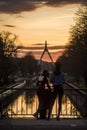 grils taking a picture with smartphone of panorama with silhouette of suspended bridge under the channel