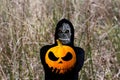 Grim reaper holding halloween pumpkin head. Man in death mask with fire flame in eyes on dry grass nature fall Royalty Free Stock Photo