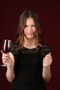 Grimace girl holding wineglass. Close up. Dark red background