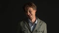 Grimacing face young man in jacket makes funny bewildered face looking at camera isolated on black background. Studio