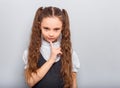 Grimacing funny thinking pupil kid girl with finger under the face in uniform thinking about and looking down on blue background