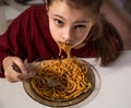 Grimacing kid girl eating tasty spaghetti on the dinner and looking up her curious ungry big eyes at the home kitchen. Closeup Royalty Free Stock Photo