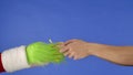 Grinchs green haired hand hold a gift box and a mans hand takes it away on a blue isolated background. Gift Royalty Free Stock Photo