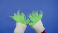 The Grinchs green haired hands against an isolated blue background. Gift kidnapper cosplay. Christmas and New Year Royalty Free Stock Photo