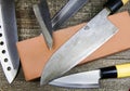 Grinding knifes: Close up of different metal japanese kitchen knifes with sharpening stone on wood table Royalty Free Stock Photo