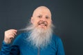 grinning bald man emphasizing the remarkable length of his white beard, set against a dark gray background, creating a striking Royalty Free Stock Photo