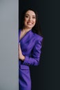 Grinning woman with her eyes wide in purple suit appearing from around a corner.