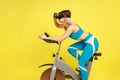 Grinning woman riding bike simulator with virtual reality headset, doing cardio training.