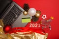 Grocery cart, laptop with bank credit card, christmas balls and pine cones and number 2021 on red background. Christmas Royalty Free Stock Photo