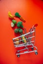 grocery consumer basket.food cost.Shopping cart with groceries on a red background.Decorative vegetables and fruits Royalty Free Stock Photo