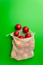 Grocery cotton net bag with red apples on a green background. Flat lay, copy space. Royalty Free Stock Photo