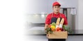 Grocery delivery courier man in red uniform and apron with grocery box with food, fresh fruit and vegetable. Deliver man handling Royalty Free Stock Photo