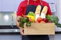 Grocery delivery courier man in red uniform with grocery box with fresh fruit and vegetable. Deliver man in red uniform and apron Royalty Free Stock Photo