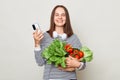 Grocery shopping at the market. Fresh vegetables for sale. Smiling brown haired woman using mobile phone for buying products Royalty Free Stock Photo